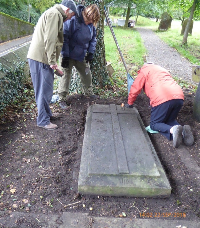 Three members of the Friends of Raikes Road Burial Ground examine a ledger stone.